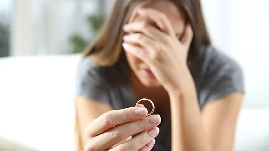 Mujer con la mano en la frente sosteniendo un anillo de boda